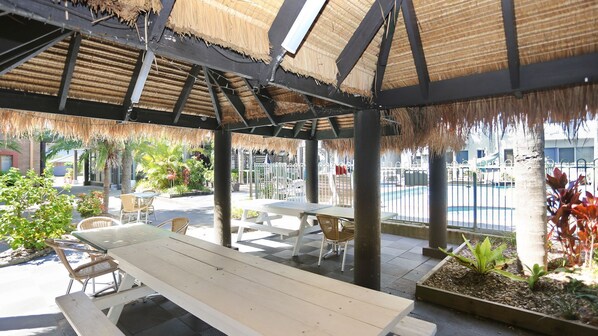 An outdoor patio area with thatched roof, wooden tables, and chairs. - Providence 3 - 100m to the Beach (Hawks Nest)