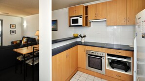 A compact kitchen with wooden cabinets, a microwave, an oven, and a refrigerator. - Providence 3 - 100m to the Beach, Ground Floor Retreat (Hawks Nest)