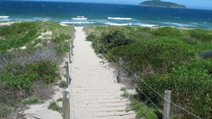 A sandy pathway leading to the ocean with a wooden fence on one side and dense greenery on the other. - Providence 3 - 100m to the Beach, Ground Floor Retreat (Hawks Nest)
