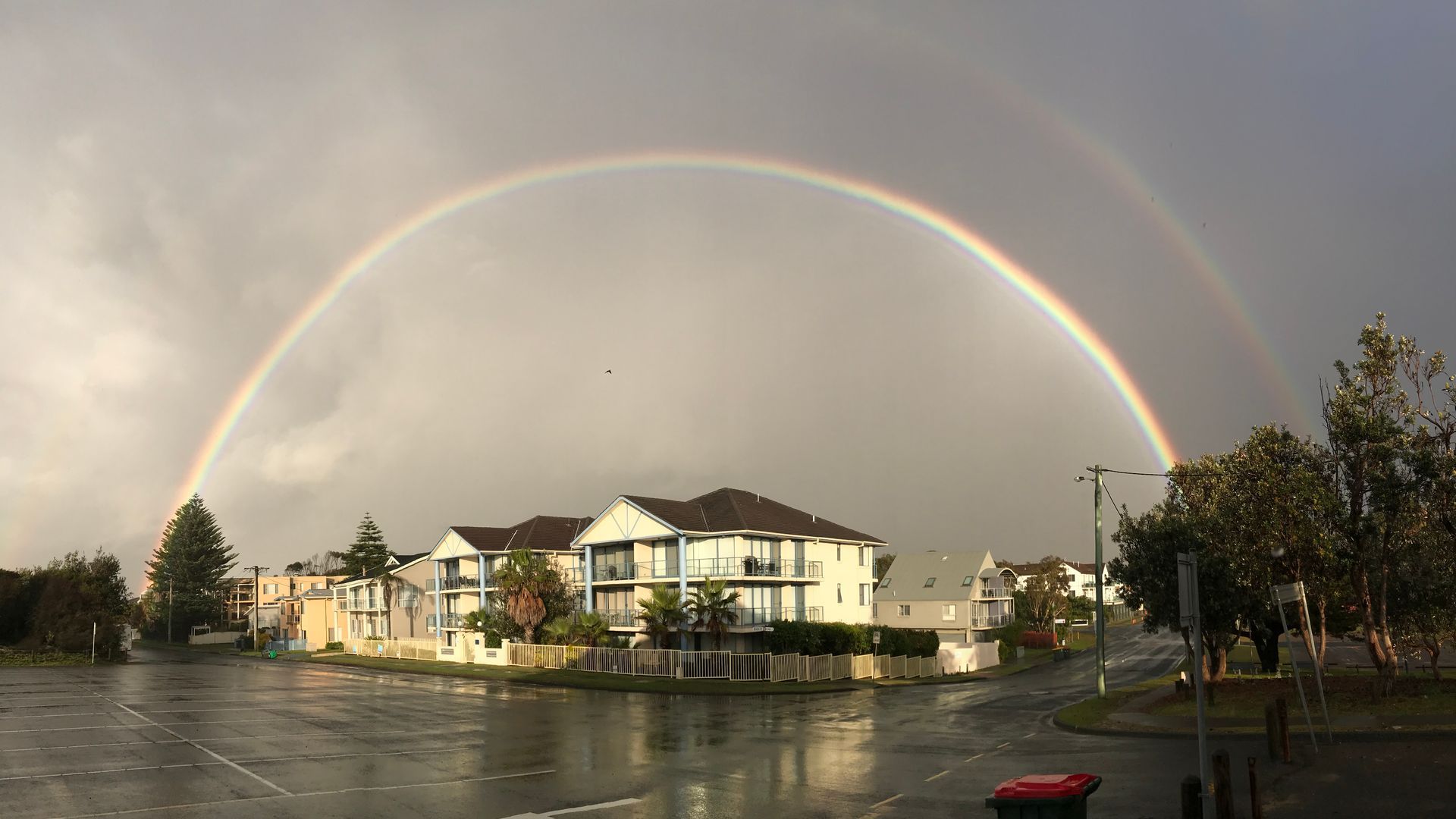 A residential area with houses, a parking lot, and a rainbow arching over the buildings.