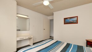 Ein Schlafzimmer mit einem Bett, einem Nachttisch, einem Spiegel, einer Tür und einem Deckenventilator.