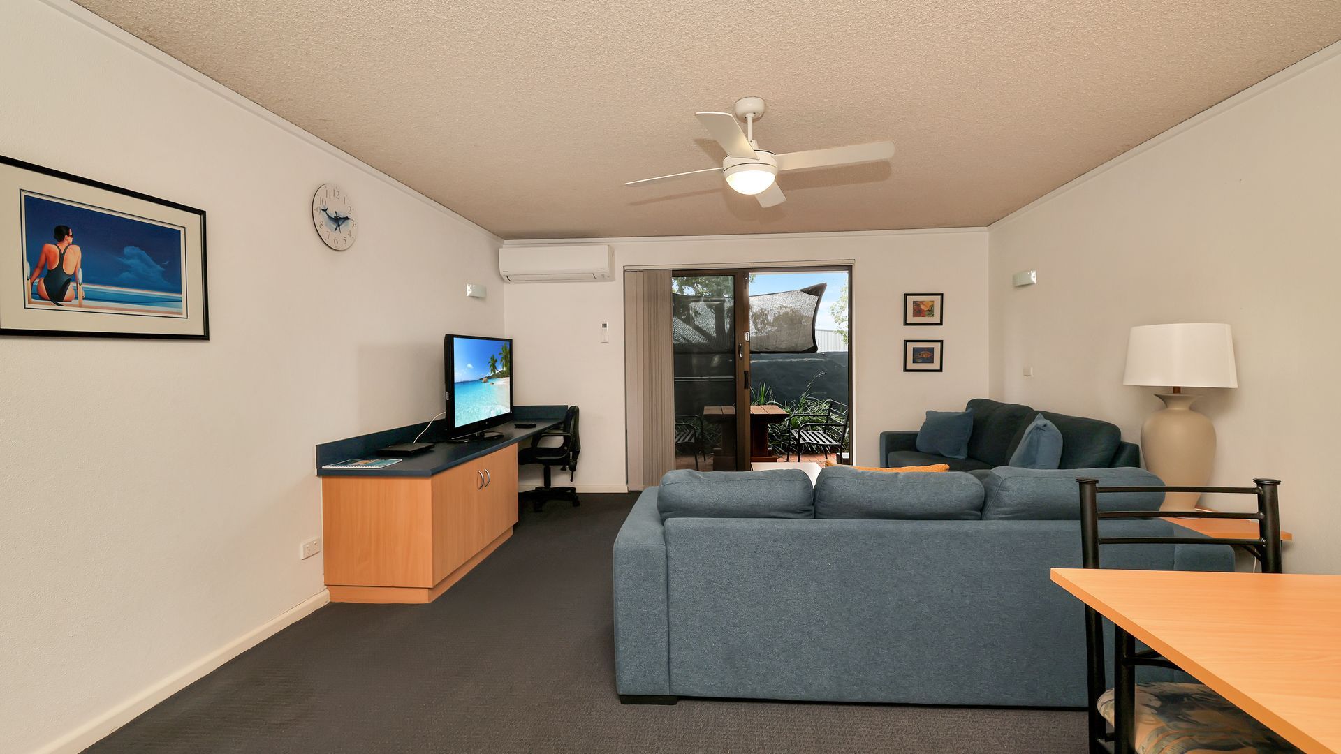 A compact living space with a sofa, a television, a desk, and a ceiling fan.