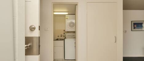 Un pasillo estrecho que conduce a una cocina pequeña con refrigerador, lavadora y un lavamanos.