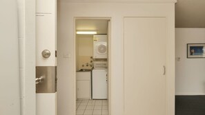 Ein schmaler Flur führt zu einer kleinen Küche mit Kühlschrank, Waschmaschine und einem kleinen Spülbecken.