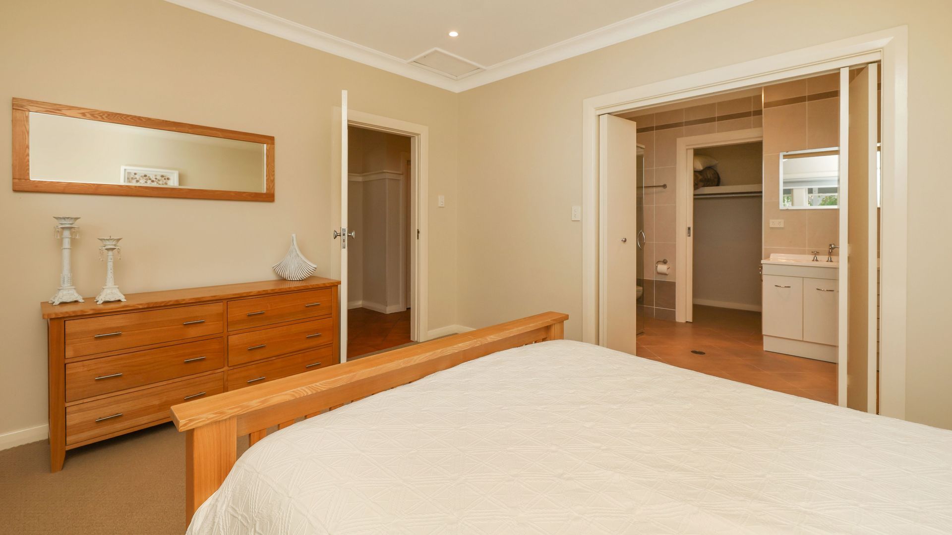 A bedroom with a wooden bed, a dresser, a mirror, and an open closet leading to a bathroom.