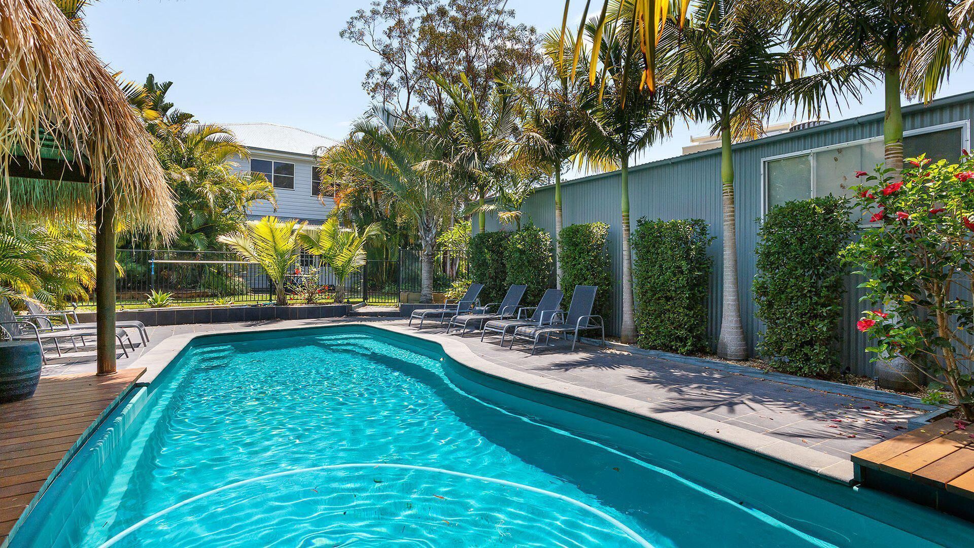 Piscina com espreguiçadeiras e plantas tropicais.