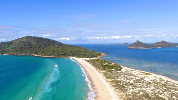 Vue aérienne d’une zone côtière avec une plage, des eaux d’un bleu limpide et deux petites îles.