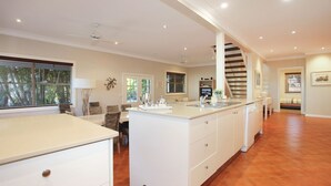 Une cuisine spacieuse dotée d’un îlot central, un coin repas avec une table et des chaises, et un escalier menant à l’étage supérieur.