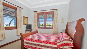A bedroom with a wooden bed, a window with curtains, a small table with a television, and a wall-mounted lamp.