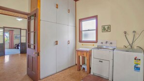 A room with a wooden door, a window with a red frame, a sink with a faucet, and a refrigerator.