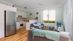 Una cucina compatta con elettrodomestici moderni, un divano grigio e un'ampia finestra con vista sul verde.