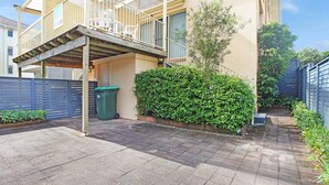 Un edificio residenziale con un patio coperto, un bidone verde e un siepe curata.