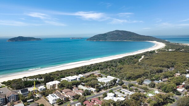Una zona residenziale sulla costa, con case, una spiaggia e una montagna sullo sfondo.