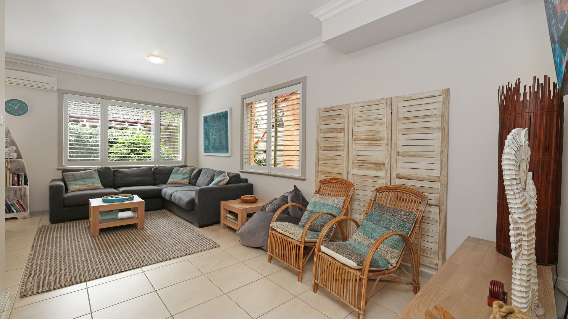 A modern living room with a sectional sofa, two wicker chairs, a coffee table, and a large window with shutters.