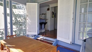 Taula i cadires de fusta en una habitació il·luminada pel sol, amb vistes a una cuina i un balcó.