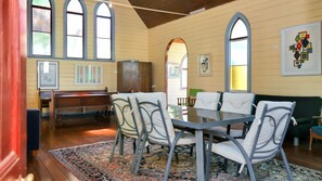 A dining area with a table, chairs, and benches. There are windows with arched tops and a patterned rug on the floor.