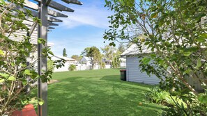 A well-maintained lawn with a wooden pergola and a small shed in a residential area.