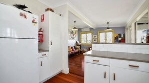 A kitchen with white cabinets, a refrigerator, and a fire extinguisher. There is a dining area with a sofa and a table.