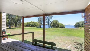 Un espace extérieur abrité, doté d’un banc en bois et d’une table, qui offre une vue sur une zone herbeuse et une étendue d’eau.