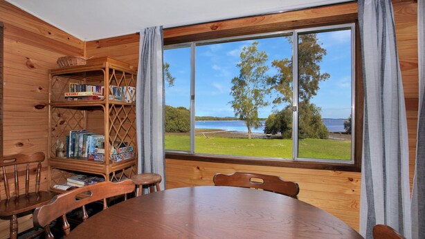 L’intérieur d’un chalet en bois, avec une grande fenêtre donnant sur un lac, une table à manger et une bibliothèque remplie de jeux.