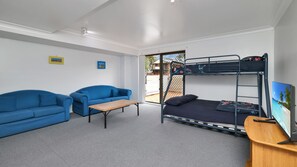 A room with bunk beds, two blue sofas, a small table, and a TV on a wooden stand. - Providence 1 - Beachside Ground Floor Apartment (Hawks Nest)