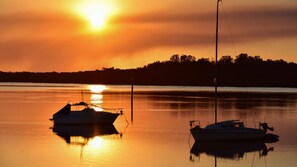 Un coucher de soleil sur un lac paisible, avec deux bateaux à l'ancre.