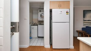 A compact kitchen with a refrigerator, washing machine, and wooden cabinets. - Providence 1 - Beachside Ground Floor Apartment (Hawks Nest)