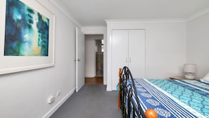 Un dormitorio con una cama, una mesita de noche, una lámpara, una puerta y un cuadro en la pared.