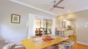 Un comedor con una mesa y sillas de madera, un ventilador de techo y vistas a la cocina a través de una puerta de cristal.