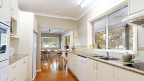Una cocina moderna con armarios blancos, horno empotrado, lavavajillas, un ventanal con vistas y una zona de comedor con mesa y sillas.