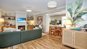 Ein modernes Wohnzimmer mit einem grünen Sofa, Holzboden, einem Kamin und einem Essbereich mit Tisch und Stühlen.