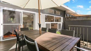 A wooden deck with a table and chairs, large windows, and a covered area with a pergola.