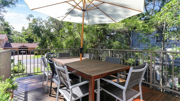 A wooden deck with a table and chairs, an umbrella, and a railing.