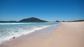 A beach with clear blue water, a sandy shore, and a mountain in the background.