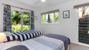 A bedroom with two beds, a window with a view of greenery, and a ceiling fan.