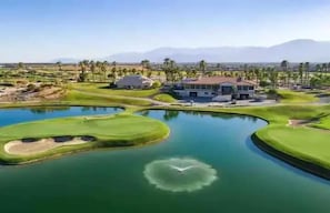 Campo de golf con un estanque, una casa y palmeras.