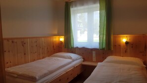 Habitación con dos camas individuales, paredes de madera, una ventana con cortinas verdes y luces fijadas en la pared.