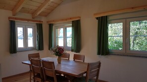 Un coin repas avec une table et des chaises en bois, un vase rempli de fleurs et de grandes fenêtres ornées de rideaux verts.