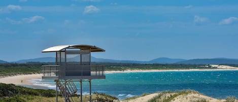Ein Rettungsschwimmturm mit Blick auf einen Strand, klares blaues Wasser und ferne Berge.