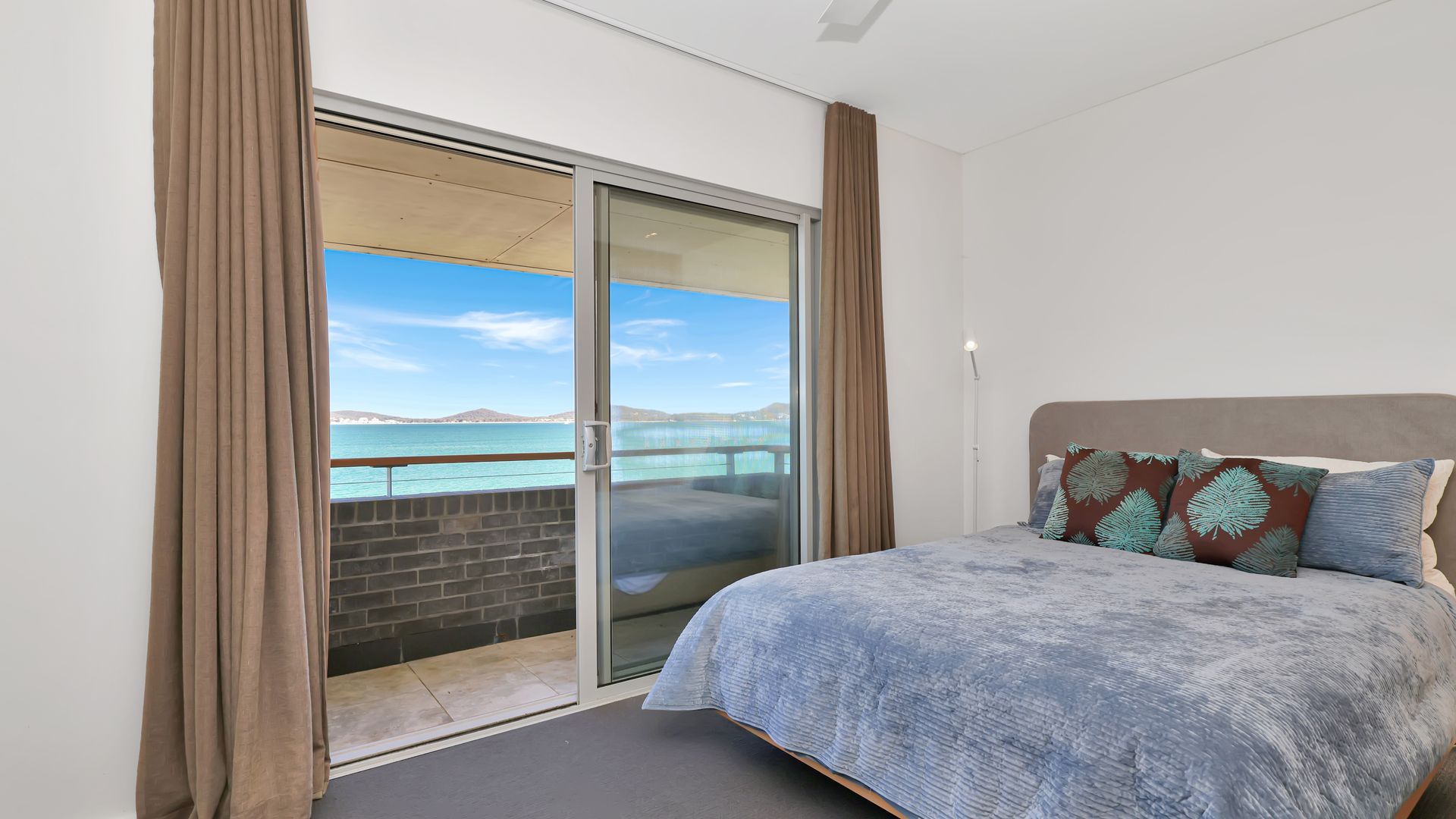 A bedroom with a bed, a view of the sea, and a sliding glass door.