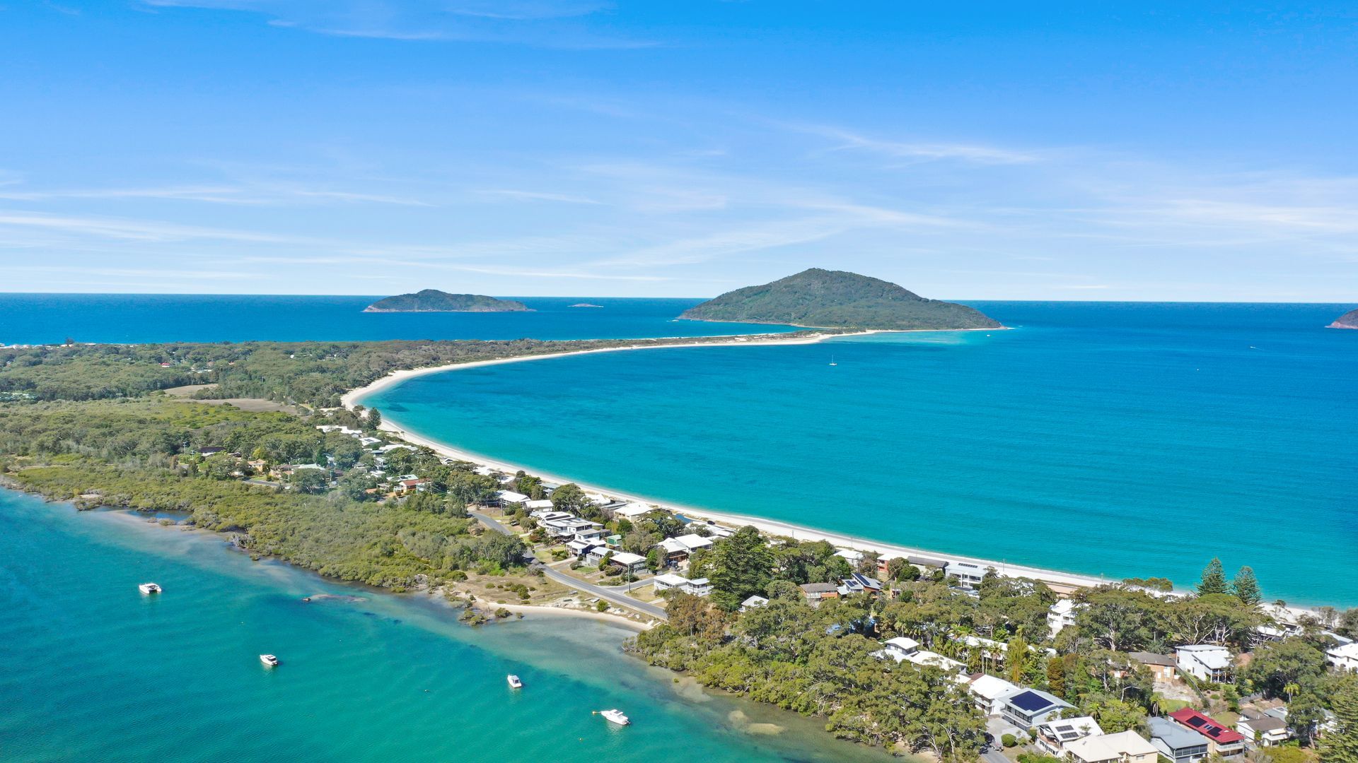 An aerial view of a coastal area with a beach, clear blue waters, and a small island in the distance.