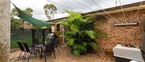 Une terrasse avec un barbecue, des sièges d’extérieur et une grande plante.