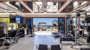 A gym with exercise equipment, a treadmill, and a view of the ocean.
