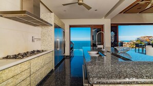 A modern kitchen with a gas stove, stainless steel appliances, and a view of the ocean through the open door.