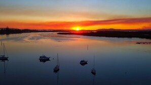 A calm body of water with several boats anchored, a sunset in the background, and a distant shoreline. - Close To The Main Surf Beach (Hawks Nest)