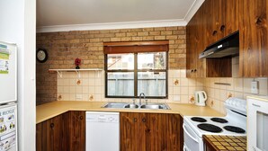 A compact kitchen with wooden cabinets, a built-in dishwasher, a stove, and a window with a view of the outside. - Close To The Main Surf Beach (Hawks Nest)
