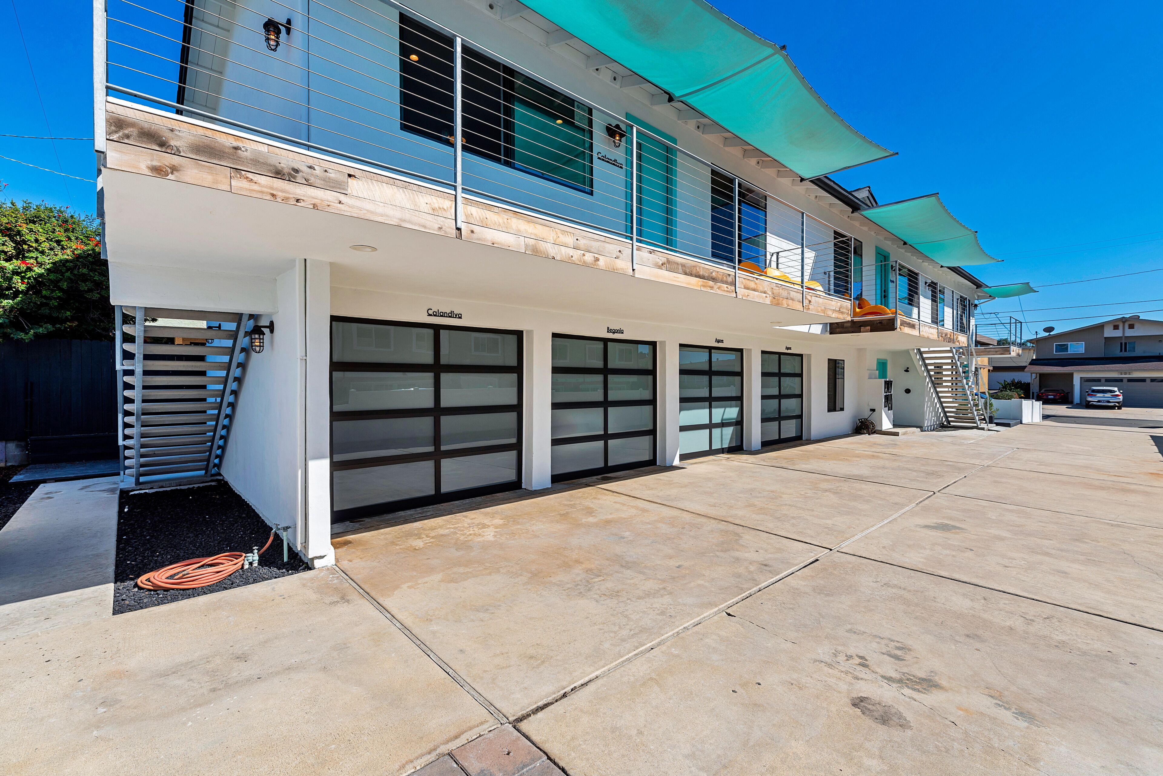 A two-story building with a garage entrance, a wooden deck, and a clear sky.