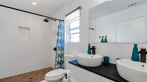 A modern bathroom with a shower, toilet, and two sinks with faucets. - Private Patio, Steps to the Sand! Walk to Village! A/C (Carlsbad)