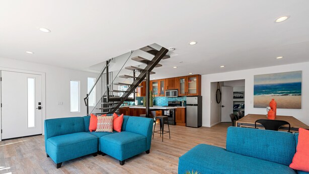 A modern living room with a blue sectional sofa, a wooden coffee table, and a staircase leading to an upper level. - Private Patio, Steps to the Sand! Walk to Village! A/C (Carlsbad)