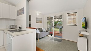 Eine moderne Küche mit integriertem Geschirrspüler, ein Essbereich mit grauem Sofa und einer Kaffeemaschine sowie ein Wohnbereich mit Fernseher und Kunstwerken an den Wänden.